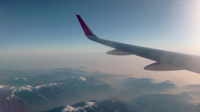 Wing of an airplane that flies over a beautiful view of the Swiss Alps. Fog and snow-capped mountain peaks, sunrise, sunlight