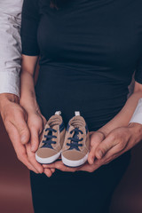 Pregnant woman and her husband holding first baby's booties close up vertical