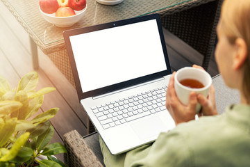 woman drinking tea and using laptop on a outdoor terrace, blank screen copy space