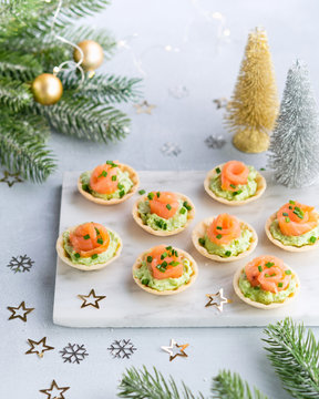 Holiday appetizer canapes with salmon avocado cream cheese on a light background with Christmas decorations. Festive table recipe ideas for New Year's and Christmas holidays.