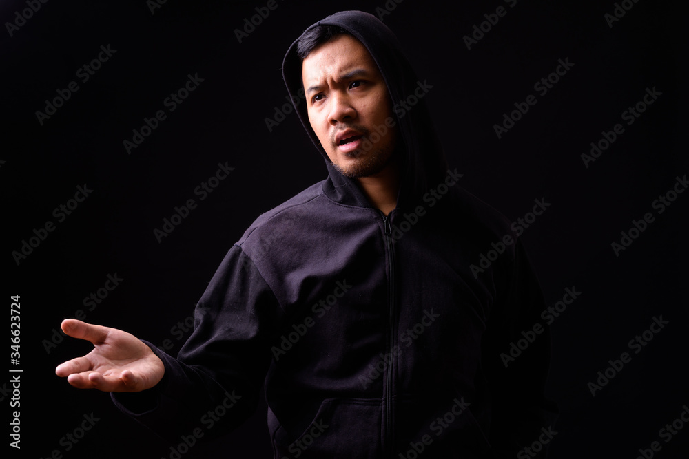 Wall mural Portrait of stressed young Asian man in hoodie complaining with hand raised