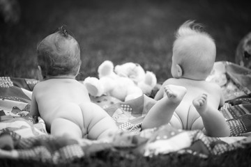 babys with bare butt lie on a blanket in the grass with toys