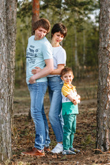 Fototapeta premium The girl hugs her husband from behind, and their son is pressed against them from behind. Parents look at the child. Everything happens in a pine forest