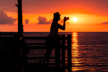 Fototapeta premium A silhouette of a girl photographer with a camera on the pier. Beautiful sunset.