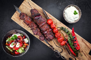 Traditionelle griechische Souvlaki Grillspieße mit Bauernsalat und Zaziki als Daufsicht auf einem Holz Board