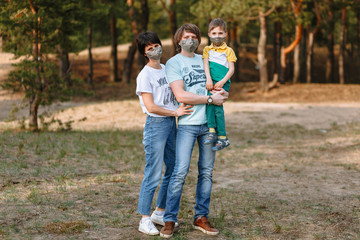 Fototapeta premium Ojciec, matka i dziecko w domowych maseczkach antywirusowych na tle lasu
