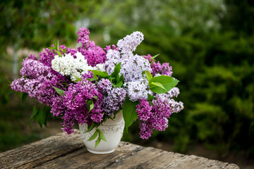 Lilac spring flowers in vase on wooden background. Tea coffee cup on table during breakfast time