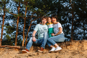 Father mother and son sit on a sandy cliff against the background of the forest