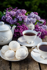 Lilac spring flowers in vase on wooden background. Tea coffee cup on table during breakfast time