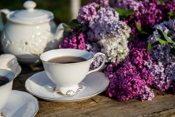 Lilac spring flowers in vase on wooden background. Tea coffee cup on table during breakfast time