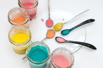 Homemade colorful paints for a baby. Glass jars with dough and food colorants and spoons on a white background. Handmade and art with kids at home.