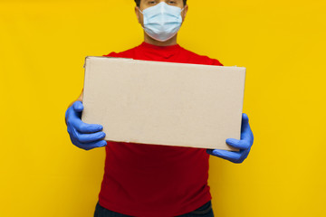 Delivery man in medical mask holding a cardbox on Yellow background.