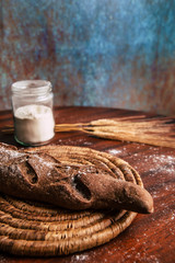 Handmade rye bread over a wooden table with spikes and a flour jar.