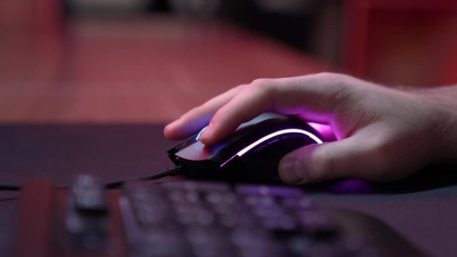 A gamer is playing in a computer club. In the frame, the hand of a gamer and a gaming mouse. Red and violet colors. ESports competitions.



