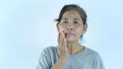 Beauty concept. An old woman applying cream on a white background. 4k Resolution.