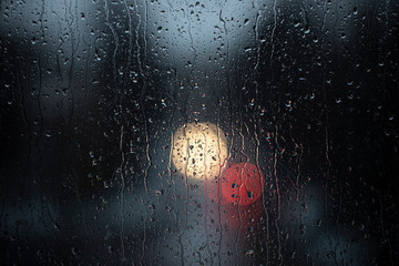 Looking through a window at a street with car's front and back light on a rainy and stormy late...