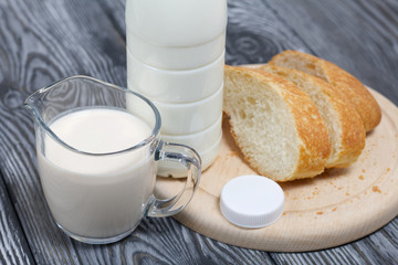 Bottle of milk, a glass of fermented baked milk and slices of ciabatta bread on a cutting board. On brushed pine boards.