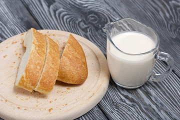 A glass of fermented baked milk and slices of ciabatta bread on a cutting board. On brushed pine boards.