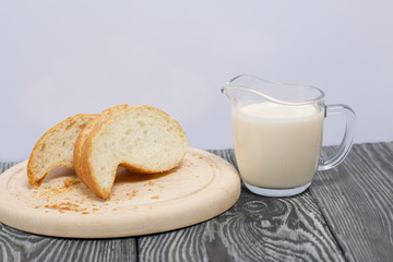 A glass of fermented baked milk and slices of ciabatta bread on a cutting board. On brushed pine boards.