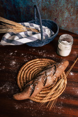 Handmade rye bread over a wooden table with spikes and cloth in a basket and a flour jar.
