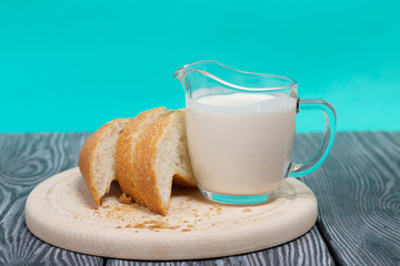 A glass of fermented baked milk and slices of ciabatta bread on a cutting board. On brushed pine boards.