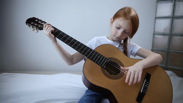 Red-haired blogger girl plays guitar on camera. a self-taught girl likes to be interesting for subscribers on her video blog.