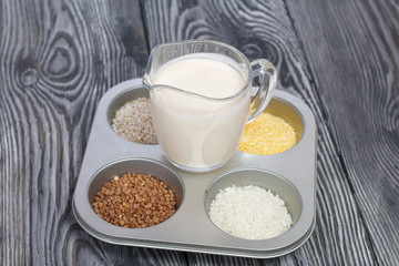 Glass with milk. Nearby in the container are cereals: buckwheat, rice, and barley corn. On brushed pine boards.