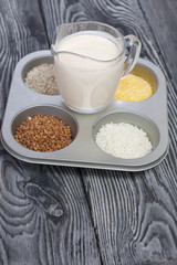 Glass with milk. Nearby in the container are cereals: buckwheat, rice, and barley corn. On brushed pine boards.