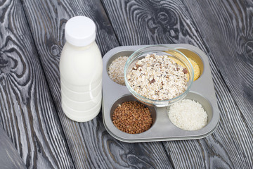 Bottle with milk. Nearby in the container are cereals: buckwheat, rice, corn and oatmeal. On brushed pine boards.