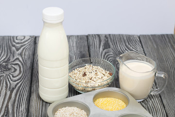 Bottle and glass with milk. Nearby in the container are cereals: buckwheat, rice, corn, barley and oatmeal. On brushed pine boards.