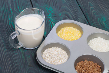 Glass with milk. Nearby in the container are cereals: buckwheat, rice, and barley corn. On brushed pine boards.
