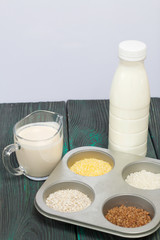 Bottle and glass with milk. Nearby in the container are cereals: buckwheat, rice, corn, barley and oatmeal. On brushed pine boards.