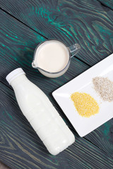 Bottle and glass with milk. Near the cottage cheese and a container with cereals: barley and corn. On brushed pine boards.