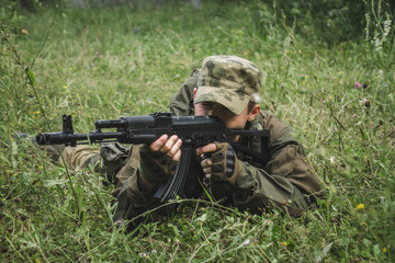 a soldier aims a rifle sitting in the bushes