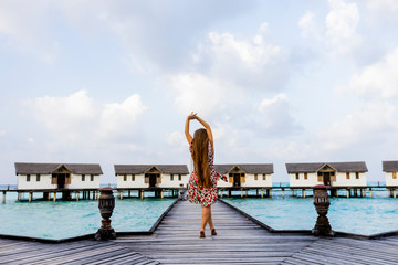 Long hair girl with arms up standing on a wooden pier and enjoying ocean