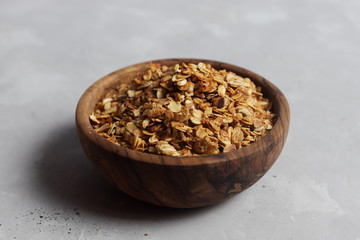 Wooden bowl, plate full of freshly cooked homemade oatmeal granola on a light gray background