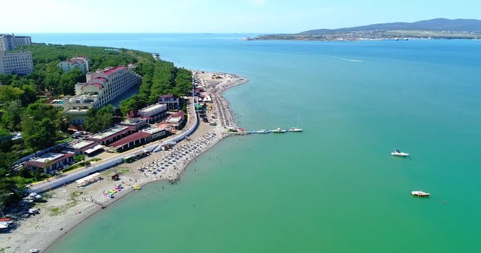 The Resort Of Gelendzhik. Flying over the beach from a bird's eye view. A pebbly beach, rows of sun umbrellas and sun loungers. People swim and sunbathe. Embankment with balustrade. A view of a large