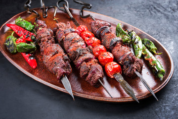 Traditional Russian shashlik on a barbecue skewer with vegetable and sumach as top view on a wooden cutting board