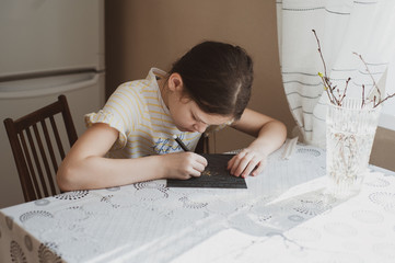 A teenager girl draws using the technique of scratching with a sharp tool of paper, drenched with ink. Waxing. Idea for quarantining a child