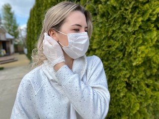 Beautiful young woman in a protective flu mask and gloves on a background of fir, looks to the side
