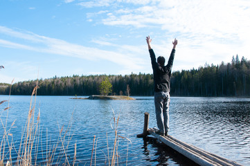 Man standing With hands up and looking at lake in forest. People and nature concept. Outdoor activity. Recreation concept. Lake in forest. Old wooden pier. People from behind 