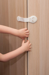 Hands of a little kid pulling the closet door closed with a special lock for child safety