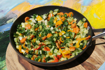 vegetable ratatouille in a frying pan, cooked vegetables of different colors in a pan, on a wooden board and colored background. Vegetarian food concept. Close-up.