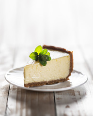 Slice of classic New York cheesecake with a sprig of mint on a plate on a wooden table. The concept of bakery and sweet cakes desserts