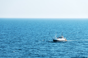 Lonely fishing ship trawler boat on ocean water. Calm clear sea sunny weather. Beautiful horizon of seascape
