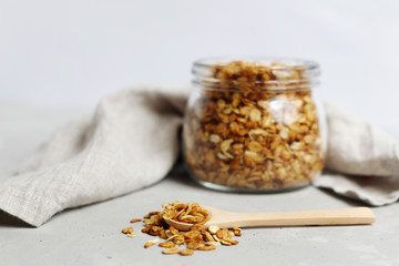 a glass jar full of oatmeal granola, in the foreground a wooden spoon with granola. Healthy...