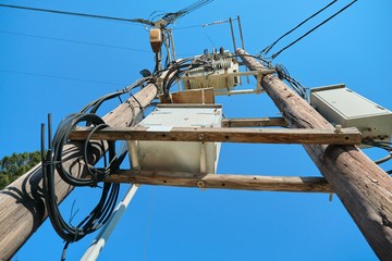Electric transformer on wooden poles, blue sky background
