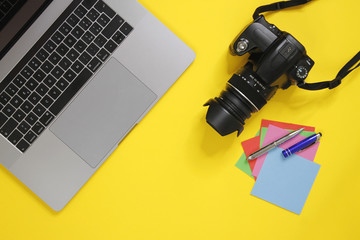 Photographer's desk with paper stickers. A yellow background with computer, camera and paper stickers of different colors