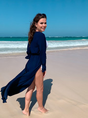 Beautiful young happy dark haired tourist girl  in blue pareo is smiling and looking to the camera. White sand beach and blue ocean on background. Holiday image