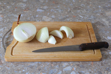 cut into several parts a large juicy peeled onion on a wooden Board and a metal knife with a brown...